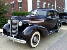 an old black car parked in front of a brick building