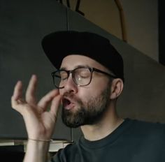 a man wearing glasses and a black hat is making an obscene gesture with his hands