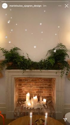 candles are lit in front of a fireplace with greenery on the mantel above it