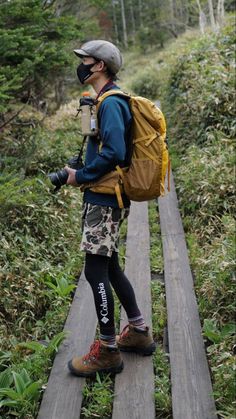 a man with a backpack is standing on a wooden bridge in the woods looking at something