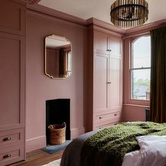 a bedroom with pink walls and green blankets on the bed, along with a chandelier