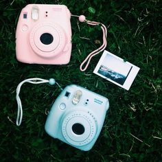 two polaroid cameras are laying on the grass next to an instax camera