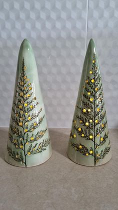 two ceramic christmas trees sitting next to each other on top of a table with yellow lights