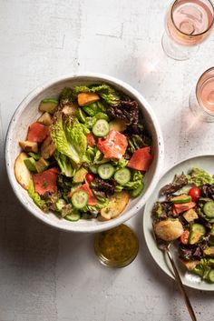 two bowls filled with salad next to wine glasses and spoons on a white table