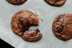 four chocolate cookies are sitting on a piece of parchment paper, with one half eaten