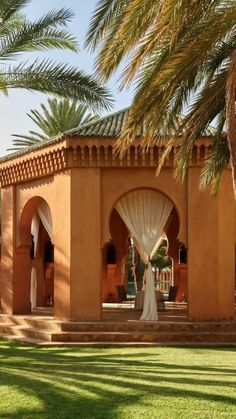 an outdoor area with palm trees and white drapes on the walls, in front of a building