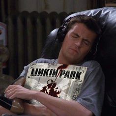 a man with headphones on sleeping in a chair holding a book that says linkin park