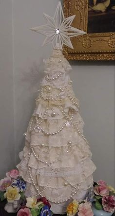 a white christmas tree decorated with pearls and bows on top of a table next to flowers