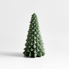 a small green christmas tree sitting on top of a white table next to a candle