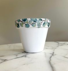 a white vase sitting on top of a marble table next to a planter with leaves painted on it