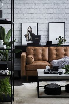 a living room filled with furniture next to a white brick wall covered in plants and pictures