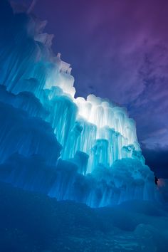 an iceberg is lit up at night with blue lights in the sky above it