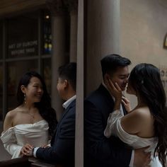 a man and woman standing next to each other in front of a window with their arms around each other