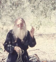 an old man with a long beard sitting on the ground holding something in his hands