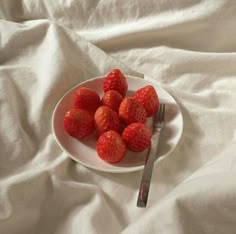 a white plate topped with strawberries next to a knife and fork on a bed