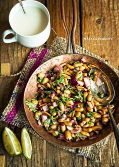 a bowl filled with beans and greens next to a cup of milk on top of a wooden table