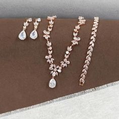 This Rose Gold Floral Bridal Jewelry Set is a perfect ensemble for the bride seeking a touch of boho charm on her special day. The set includes a chunky necklace, teardrop pendent choker, and a leaf bracelet, all adorned with sparkling cubic zirconia stones that catch the light beautifully. CZ NECKLACE: Necklace Length: approx 16 1/2 inches. Featuring a floral design that adds a touch of nature's elegance to your bridal look. Crafted with high-quality cubic zirconia stones and copper, this necklace is designed to sparkle under any light. CZ EARRINGS: These floral design earrings are a beautiful addition to the set, suitable for any occasion. The earring length is about 1 3/8" (3.5cm), with a bottom teardrop size of 1/2"H x 3/8"W (1.5cm x 1cm), offering a delicate balance of size and style. Wedding Jewelry Rose Gold, Bohemian Teardrop Necklace For Weddings, Bohemian Teardrop Jewelry For Wedding, Rose Gold Teardrop Jewelry Sets For Wedding, Rose Gold Teardrop Wedding Jewelry Sets, Bohemian Rose Gold Jewelry For Wedding, Rose Gold Teardrop Bridal Necklace, Bohemian Wedding Jewelry With Matching Earrings, Bohemian Wedding Necklace With Matching Earrings