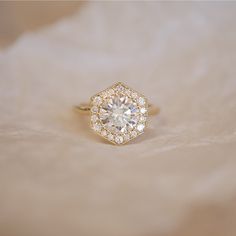 a diamond ring sitting on top of a white furnishing surface with the center stone surrounded by small round diamonds