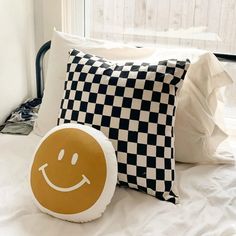 a smiley face pillow sitting on top of a bed next to a black and white checkered pillow