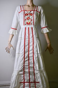 "This dress is so special. It is a vintage 60s/70s Mexican pin tucked white dress. The dress has a square neckline, that is trimmed with red ribbon and small lace ruffles, is fitted to the waist with a floral embroidered bodice that is also finished on the side with red ribbon, it has 3/4 sleeves with a flared lace cuff and red ribbon trim, The skirt is a long maxi skirt that is quite full, it has a front and back center panel with red ribbon running down the length, coming off the front panel i White Floral Embroidered Vintage Dress, White Folk Style Wedding Dress, White Lace Cottagecore Vintage Dress, Bohemian Embroidered Cotton Dress For Wedding, Bohemian Cotton Embroidered Dress For Wedding, Bohemian Embroidered Cotton Wedding Dress, Bohemian Cotton Embroidered Wedding Dress, White Cotton Prairie Dress For Wedding, White Bohemian Embroidered Dress With Ruffles