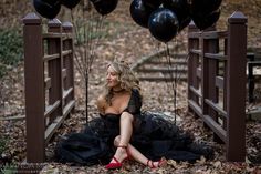 a woman in a black dress sitting on a bridge with balloons floating over her head