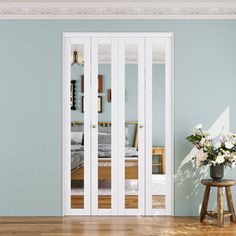 an empty room with blue walls and wooden floors, white french doors leading to a bed