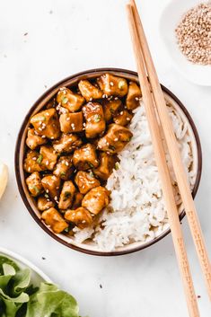 a bowl filled with chicken and rice next to chopsticks on top of a table