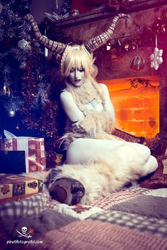 a woman dressed as a demon sitting in front of a christmas tree