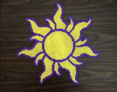 a yellow and purple cross stitched sun on a wooden surface