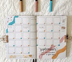 an open planner book with markers and pens on the cover, next to it is a calendar