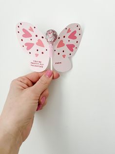 a hand holding a candy bar shaped like a butterfly on top of a white wall