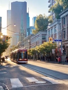 a red and white train traveling down a street next to tall buildings in the city