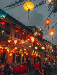 people are sitting at tables under lanterns in the evening