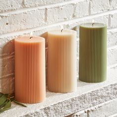 three candles sitting on top of a white brick wall