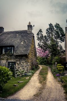 an old stone house with a thatched roof and door is on the side of a gravel road