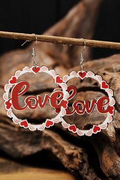 two wooden earrings with the word love hanging from it's earwires on top of a piece of wood