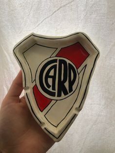 a hand holding up a small white and red plate with the letter g r on it