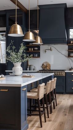 a kitchen with dark blue cabinets and gold pendant lights hanging from the ceiling, along with bar stools