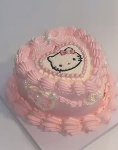 a hello kitty cake with pink icing and pearls on it's edges, sitting on a white surface