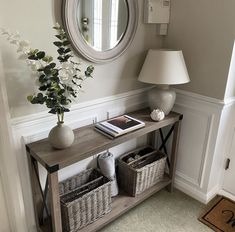 a table with baskets under a mirror next to a lamp and vase on the floor