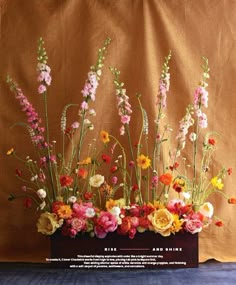 a vase filled with lots of colorful flowers on top of a wooden table next to a brown wall