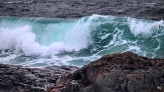 an ocean wave breaking over rocks on the beach