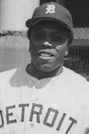 a black and white photo of a baseball player wearing a detroit tigers uniform in front of a fence