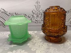 two glass vases sitting next to each other on a white tablecloth covered surface