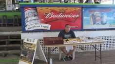 a man sitting at a table in front of a budweiser sign and posters