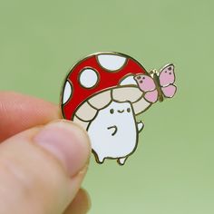 a hand holding a mushroom brooch with a pink butterfly on it's back