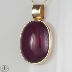 "11.8 cts. of beautiful red Ruby in a handmade 14 kt gold bezel setting with a hand forged bail. The pendant measures 23 mm long by 13 mm wide. The bail opening is 3 mm. Ruby is a birthstone for July. Mined in Mozambique HGF. Ruby is one of the highest valued colored gemstones. Ruby has been prized for centuries because of its excellent hardness along with its treasured rich red hue and vitreous luster. Ruby is a variety of corundum that gets its red color from chromium. Ruby typically displays Polished Yellow Gold Ruby Jewelry, Formal Ruby Jewelry With Oval Cabochon, Oval Cabochon Ruby Jewelry For Formal Occasions, Formal Oval Cabochon Ruby Jewelry, Red 14k Gold Oval Pendant Jewelry, Ruby Cabochon Pendant Jewelry, Red Oval Cabochon Jewelry With Polished Finish, Red Round Pendant Jewelry With Bezel Setting, Red Pendant Jewelry With Bezel Setting