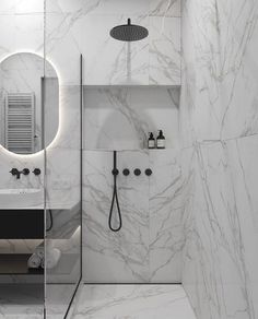 a bathroom with marble walls and flooring is shown in black and white, while the shower has a round mirror above it