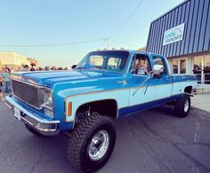 a blue pickup truck parked in front of a building with people standing around the window