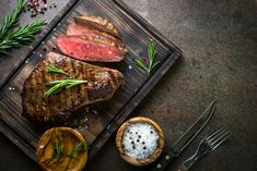 two steaks on a cutting board with salt and pepper